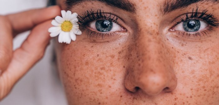 Porentief reines Frauengesicht mit blauen Augen und Gänseblümchen als Deko im Haar