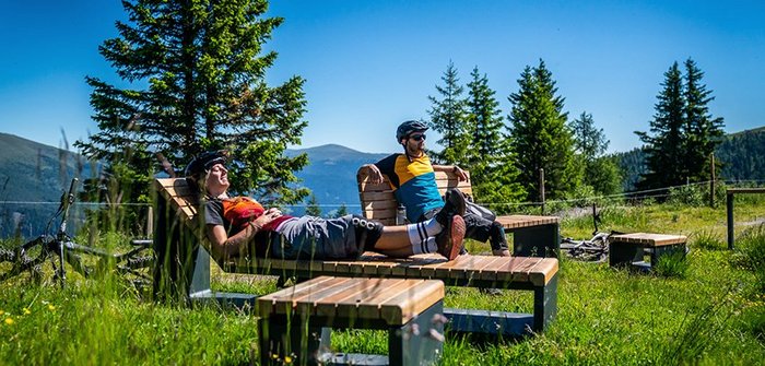 Bike-Pärchen am Panorama-Rastplatz entlang des Flow Country Trails, Jausenpause mit Bergpanorama in den Alpen