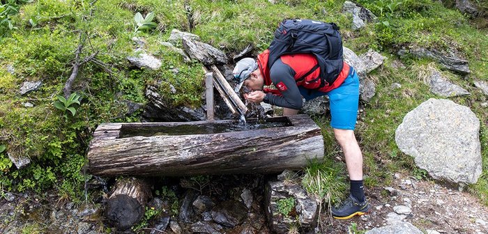 Ein Mann trinkt Wasser an einer Wasserstelle.