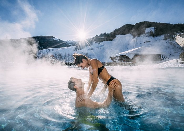 Paar im Außenbecken des Thermal Römerbads, mit Blick auf die Piste im Skigebiet