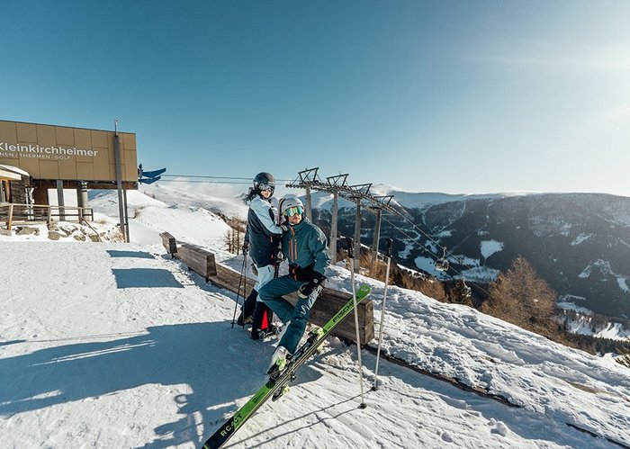 Skifahrer an der Panoramabank auf der Brunnachhöhe, direkt an der Bergstation Biosphärenparkbahn Brunnach, Aussicht in die Nockberge und den Biosphärenpark, Blick in das Dorf Bad Kleinkirchheim