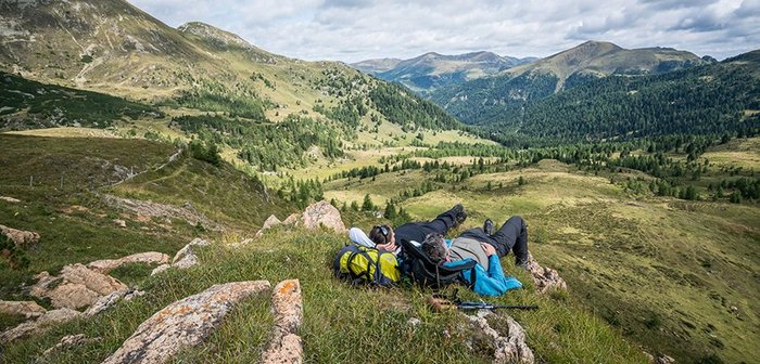 Zwei Personen liegen auf einer Wiese und beobachten eine traumhafte Bergkulisse.