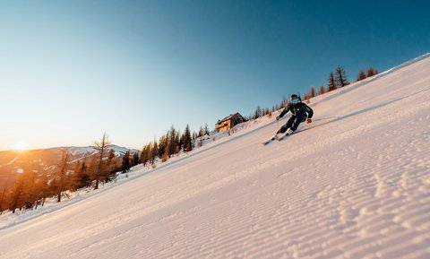 Skifahrer auf präparierter Piste in den österreichischen Alpen bei Sonnenuntergang