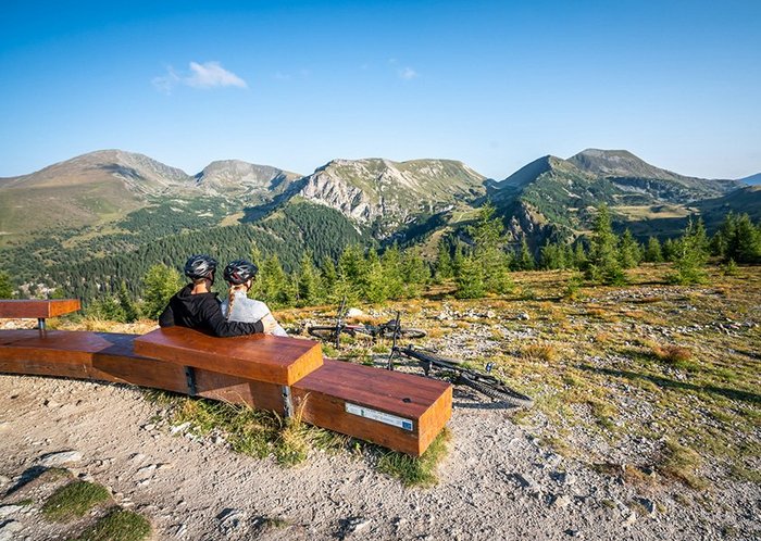 Biker-Paar auf der Panoramabank, mit Sicht auf den UNESCO Biosphärenpark Kärntner Nockberge