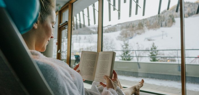 Eine Frau liegt auf einer Liege und ließt ein Buch.