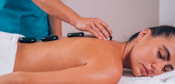 Eine Person platziert Hot Stones auf dem Rücken einer Frau.
