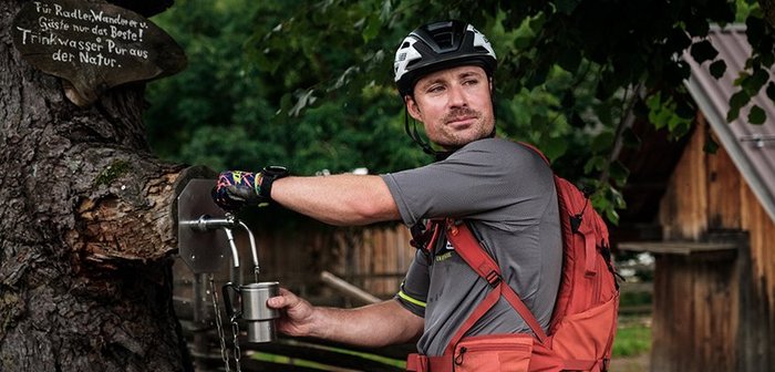 Ein Mountainbiker füllt an einem Wasserhahn einen Becher mit Wasser.