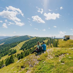 Ein Mann und eine Frau sitzen in einer Wiese und beobachten die traumhafte Natur.