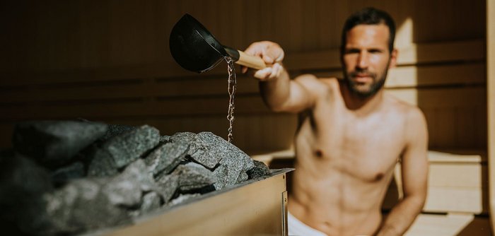 Ein Mann gießt Wasser auf heiße Steine in der Sauna.