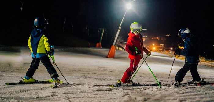 Drei Kinder beim Nachtskifahren auf der Piste.