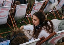 Frau mit Kopfhörern sitzt in Liegestuhl bei Open-Air-Veranstaltung in Wien