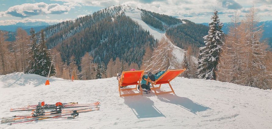 Schifahrer auf Liegestühlen im Schnee mit Bergkulisse, Kärnten