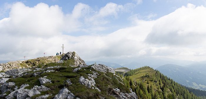 Bergpanorama mit Gipfelkreuz und Wolkenhimmel.